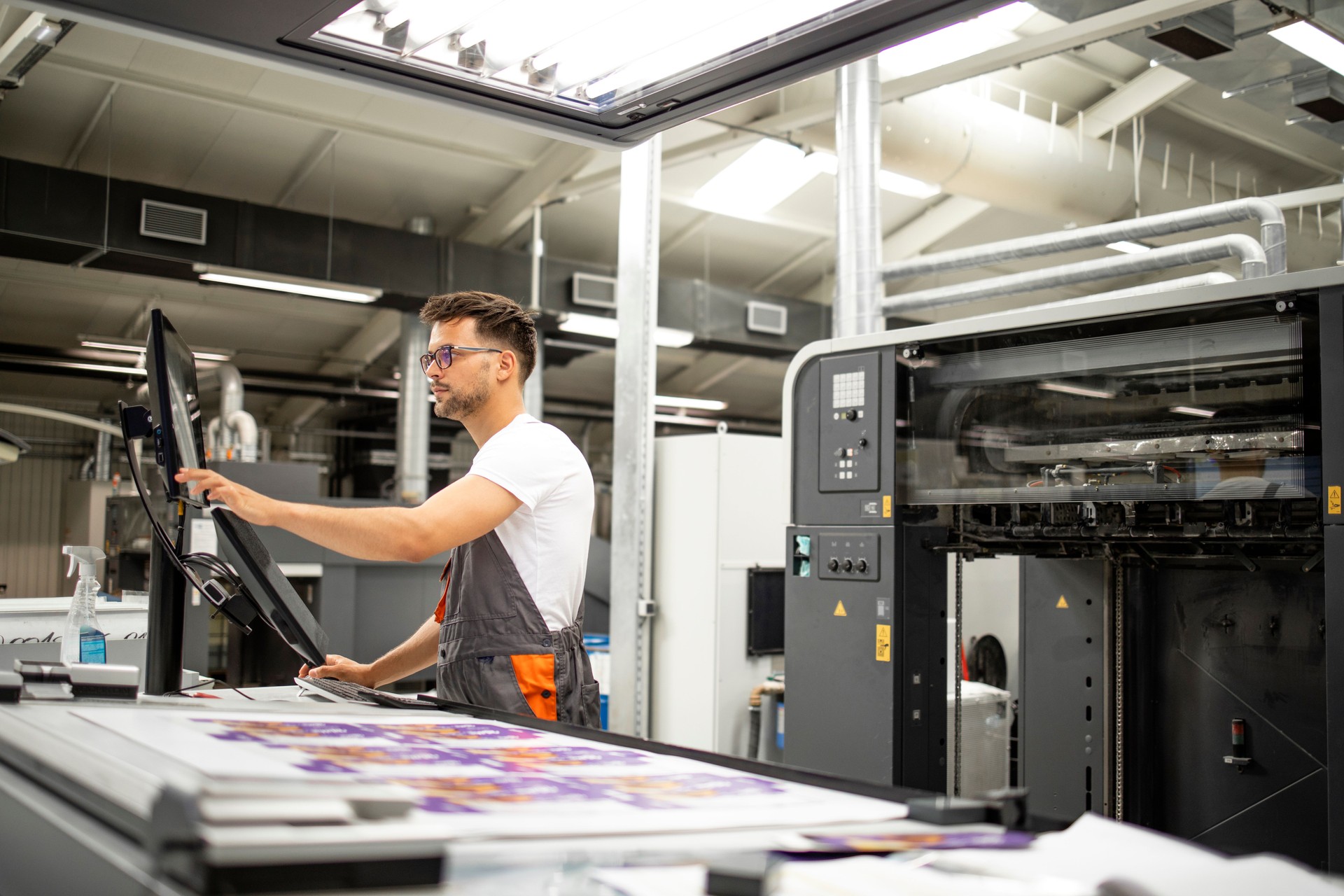 Print house worker setting parameters on modern offset printing machine.
