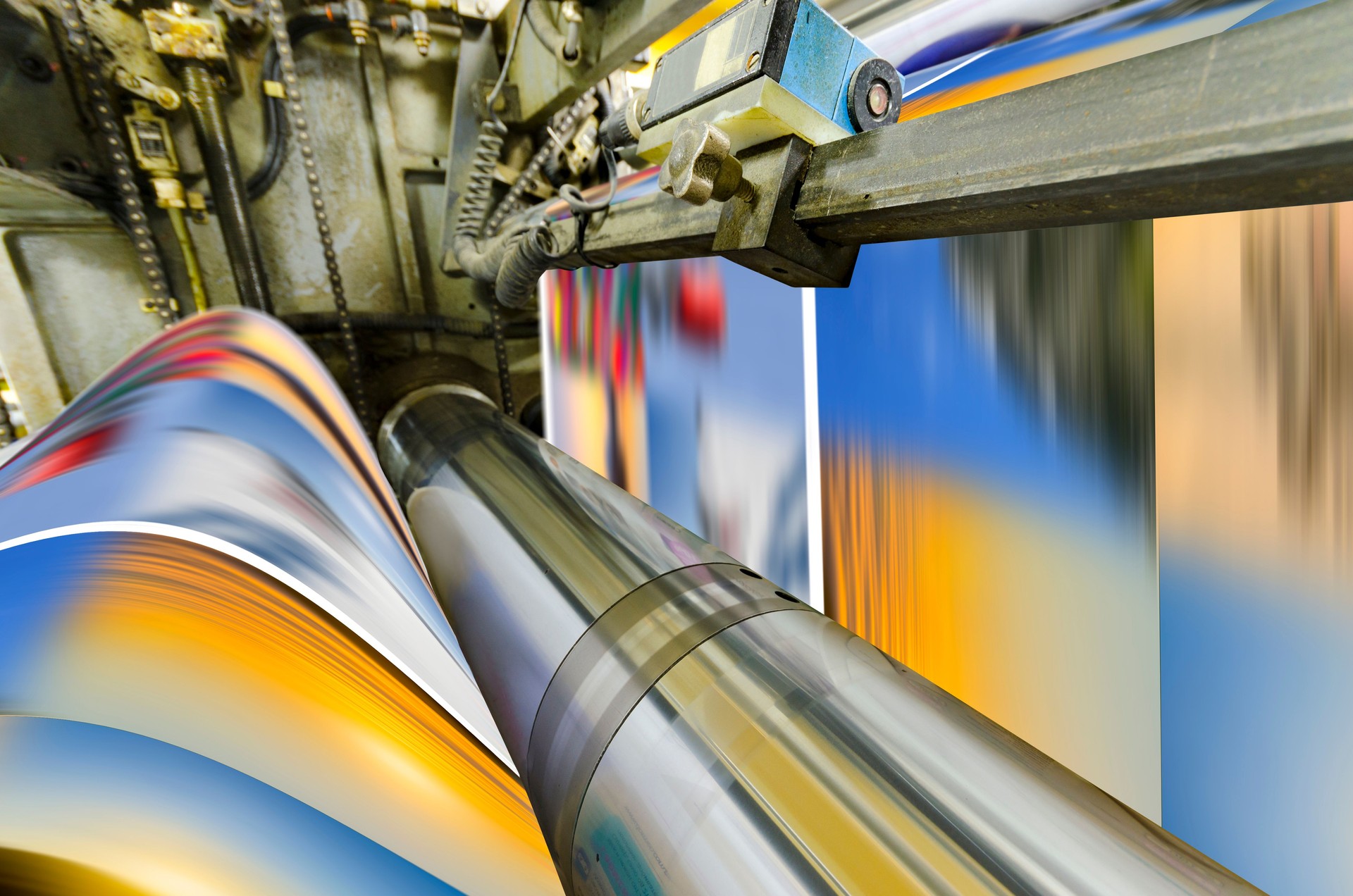 A large offset printing press running a long roll off paper over its rollers at high speed