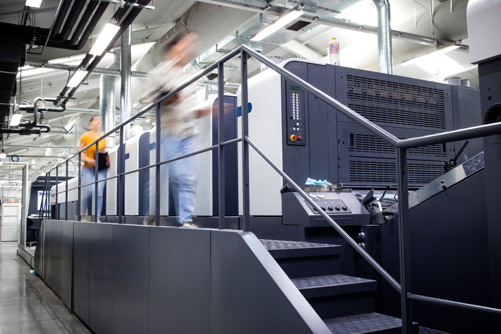 Printing factory interior with modern offset printing press machine and busy people working around.